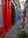 People including man on mobile phone in narrow alleyway of different coloured frontages and doors