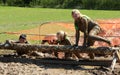 People Jumping over muddy logs in the Mud while competing in a Mud Run