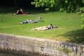 People laying on green grass relaxing and sunbathing by Spree river in hot summer.