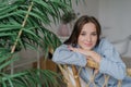 People, leisure concept. Beautiful European woman dressed in stylish clothes, sits on wooden chair near green plant, looks positiv