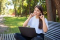 Young happy student girl sitting on bench in park with laptop, in wireless headphones Royalty Free Stock Photo