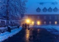 People at lighted monastery entrance, snowy misty winter season night scene