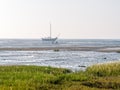 People looking for shellfish in mudflats and dried out sailboat at low tide, Waddensea near Schiermonnikoog, Netherlands