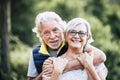 People in love at old age - couple of caucasian cheerful happy senior smile and hug in relationship - green defocused forest in