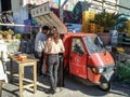 People near a classic red Piaggio APE three-wheeler parked on the street