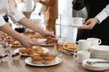 People near table with dishware and different delicious snacks during coffee break, closeup