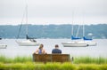 People on park bench with yachts and water in background