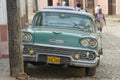 People pass vintage American car parked at the street in Trinidad, Cuba.