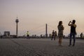 People photographing the Rhine tower as others walk by in Dusseldorf, Germany.