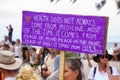 People protesting Covid-19 vaccine mandates, woman holding large purple placard saying health does not always come from medicine.