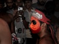 people in public taking photos of a theyyam artist decorated with bright face paint