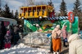 People queue up for the Crazy Bus attraction in the central city park against the backdrop of trees in the spring