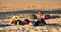 People relaxing on the beach. A woman reading a book in the background. A couple talking in f Royalty Free Stock Photo