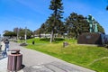 People relaxing on green grass in the park near a white wooden pergola surrounded by lush green trees with blue sky