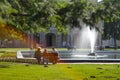 People are resting on the bench near the fountain