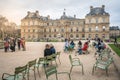 People resting on iconic green chairs at Jardin du Luxembourg gardens in front of the French Senate building in Paris France