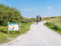 People riding bikes and information board in dunes of nature reserve Het Oerd on West Frisian island Ameland, Friesland,