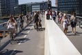 People riding bikes and walking on a modern pedestrian and bicycle bridge in city center by the harbor in sunny weather.