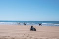 People riding quadbike and horses along shoreline at beach against clear sky