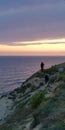 People on the rock against the sunset sea landscape. The sea and sky are painted in pink and purple colors. Symbolic background