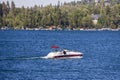 People sailing a red and white motorboat across the rippling blue waters of Lake Arrowhead with boat docks, homes