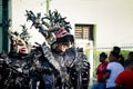 People in scary black demon costumes walk by city street at dominican carnival