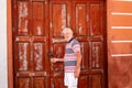 People senior with white beard and hair tries to open an old red door closed by lock. spanish home with red windows and doors made Royalty Free Stock Photo