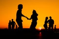 People silhouettes dancing against warm sunset orange sky