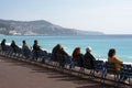 People sit on the famous blue chairs on the Promenade des Anglais, watch the azure sea and enjoy the warm sunshine. Rest and relax