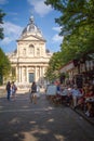 People sit at tables on the summer terrace of the cafe in front of the main entrance of university Sorbonne in Paris