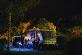 People sit under an awning and watch TV, Night view of the parking lot for a motorhome, camper van, campsite camp for sleeping and