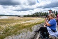 People sitting on benches around the Old Faithful Geyser waiting for it to erupt