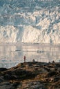 People sitting standing in front of huge glacier wall of ice. Eqip Sermia Glacier Eqi glacier in Greenland called the