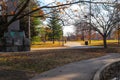 People sitting in a swing in the park surrounded by lush green trees and plants and autumn colored trees and other people walking