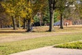 People sitting in a swing in the park surrounded by lush green trees and plants and autumn colored trees and other people walking