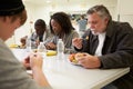 People Sitting At Table Eating Food In Homeless Shelter