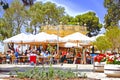 People sitting together at tables and chairs having drinks and food in a outdoor cafe in a park in Valletta Malta