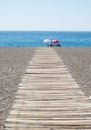 Wooden path leading to people sitting on beach under umbrellas