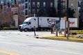 People standing on a corner at an intersection with a white semi truck turning the corner surrounded by apartment buildings