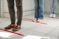 People standing in line behind taped floor markings for social distance indoors, closeup. Coronavirus pandemic
