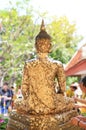People sticking the gold foil sheet on back Buddha statue for respect