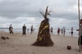 People and the Straw Scarecrow stand on a sandy beach on the ocean shore during a ceremony for good weather and good fishing