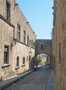 People on the street of the knights of rhodes lined with medieval buildings and an archway joining buildings