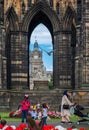 People strolling in Princes Street Gardens and view of The Balmoral through Scott Monument in Edinburgh, Scotland Royalty Free Stock Photo