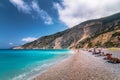 People sunbathing on beach by the blue seascape surrounded by rocky mountains in Cephalonia, Greece