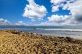 People surfing in vast blue ocean water with waves rolling into the beach with clear blue sky and powerful clouds at sunset Royalty Free Stock Photo