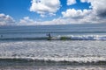 People surfing in vast blue ocean water with waves rolling into the beach with clear blue sky at sunset Royalty Free Stock Photo