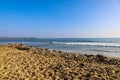 People surfing in vast blue ocean water with waves rolling into the beach with clear blue sky and powerful clouds at sunset Royalty Free Stock Photo