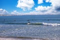 People surfing in vast blue ocean water with waves rolling into the beach with clear blue sky at sunset Royalty Free Stock Photo