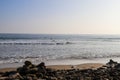 People surfing in vast blue ocean water with waves rolling into the beach with clear blue sky at sunset Royalty Free Stock Photo